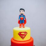 Colorful superhero cake featuring a fondant Superman figurine on top, perfect for themed parties.